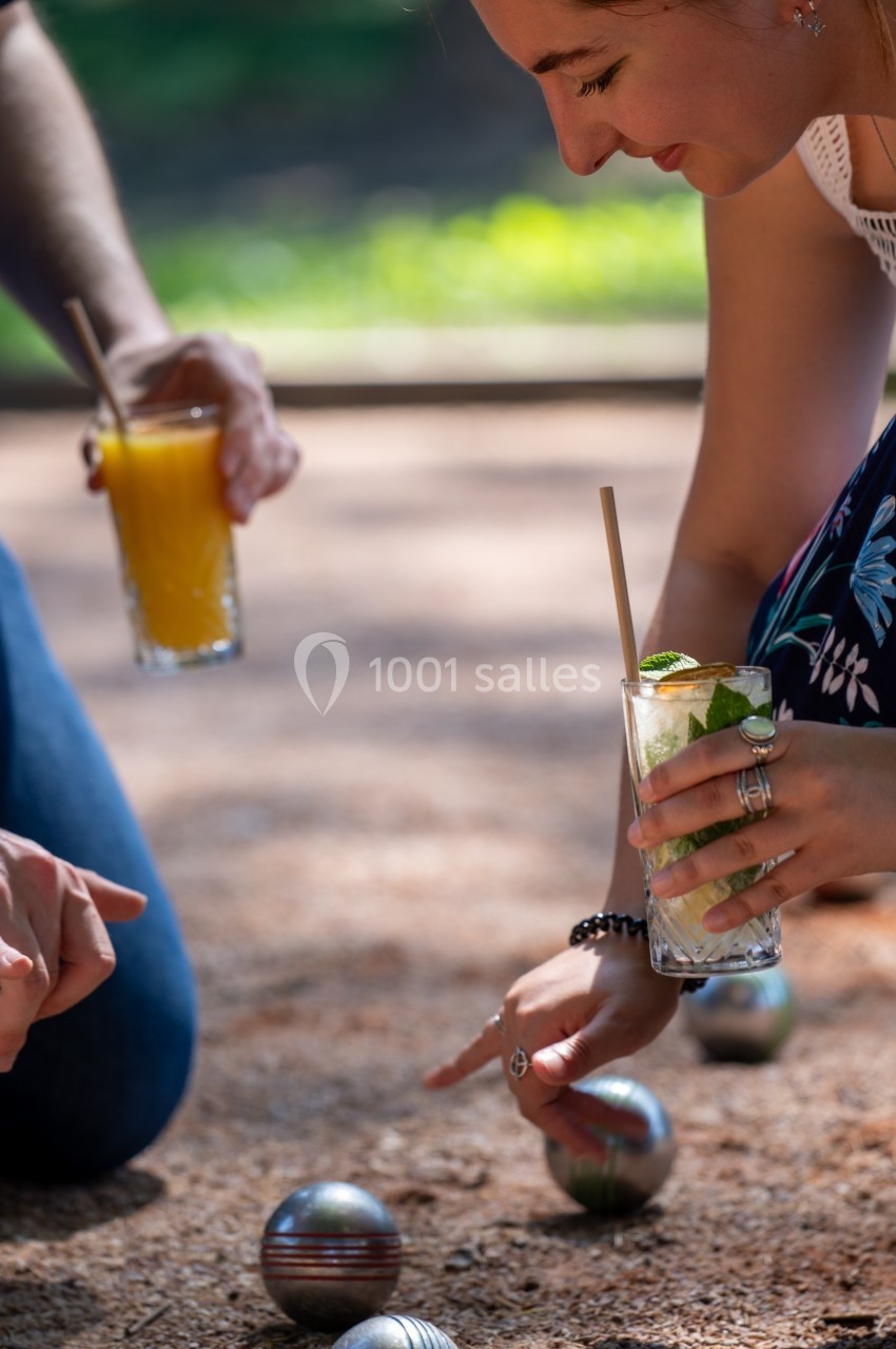 Personnes jouant à la pétanque en extérieur, tenant des boissons fraîches dans un cadre ensoleillé.