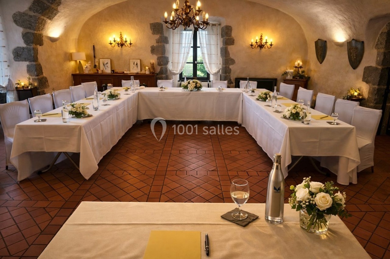 Salle de réunion élégante avec tables en U, nappes blanches, décorations florales et éclairage chaleureux.