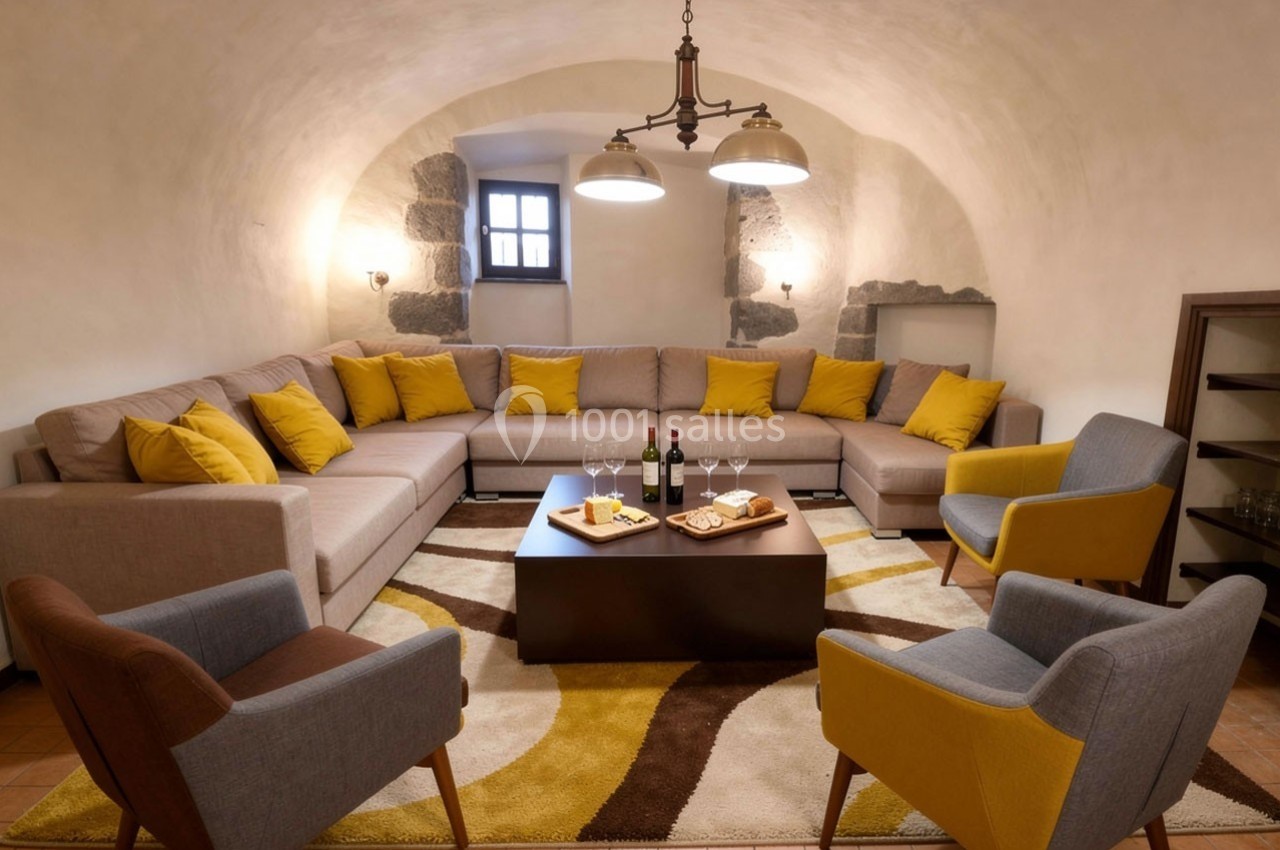 Salon voûté avec canapé d'angle beige, coussins jaunes, fauteuils modernes et table basse avec boissons et snacks.