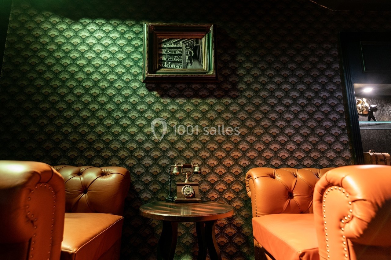 Deux fauteuils en cuir marron encadrent une table avec un téléphone vintage, devant un mur texturé et un tableau.