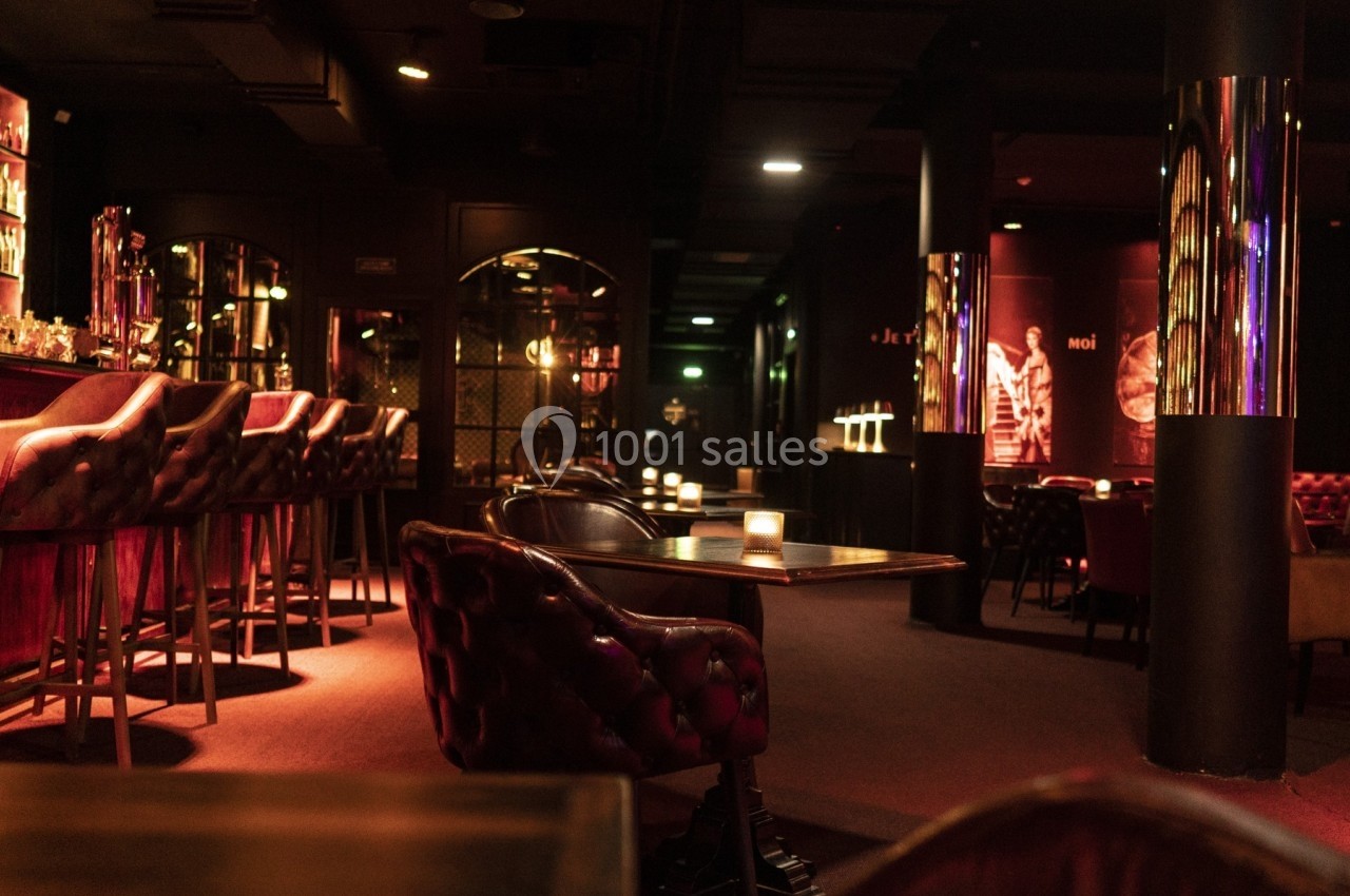 Salle de bar tamisée avec fauteuils en cuir, tables en bois et éclairage chaleureux.