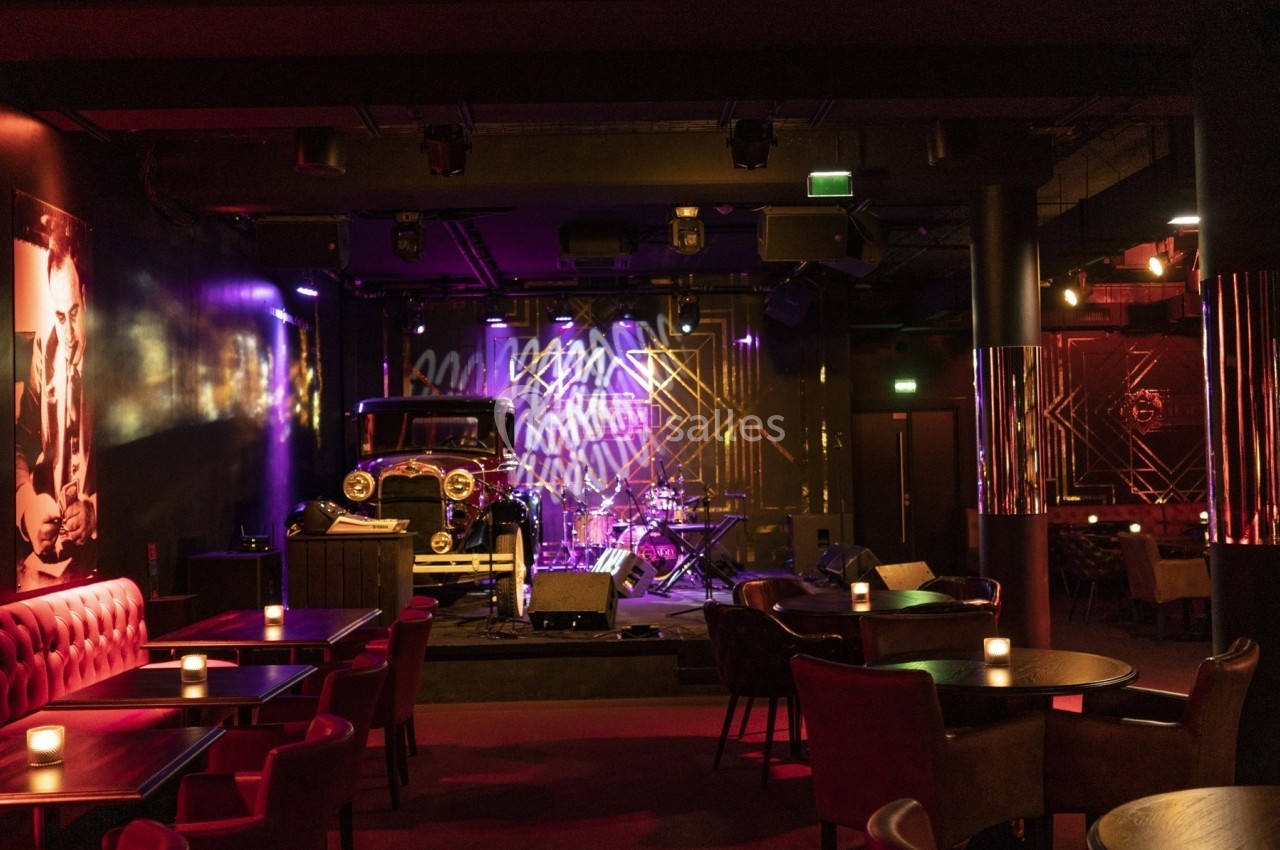 Salle de concert intimiste avec tables éclairées par des bougies, scène équipée d'instruments et éclairages colorés.