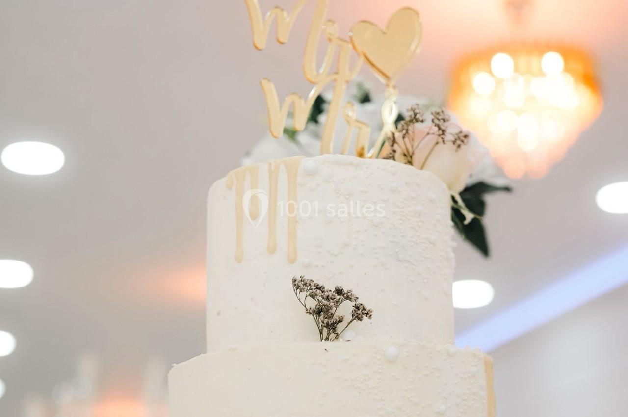 Gâteau de mariage à deux étages décoré de fleurs séchées et d'un topper doré, sur un support en bois.