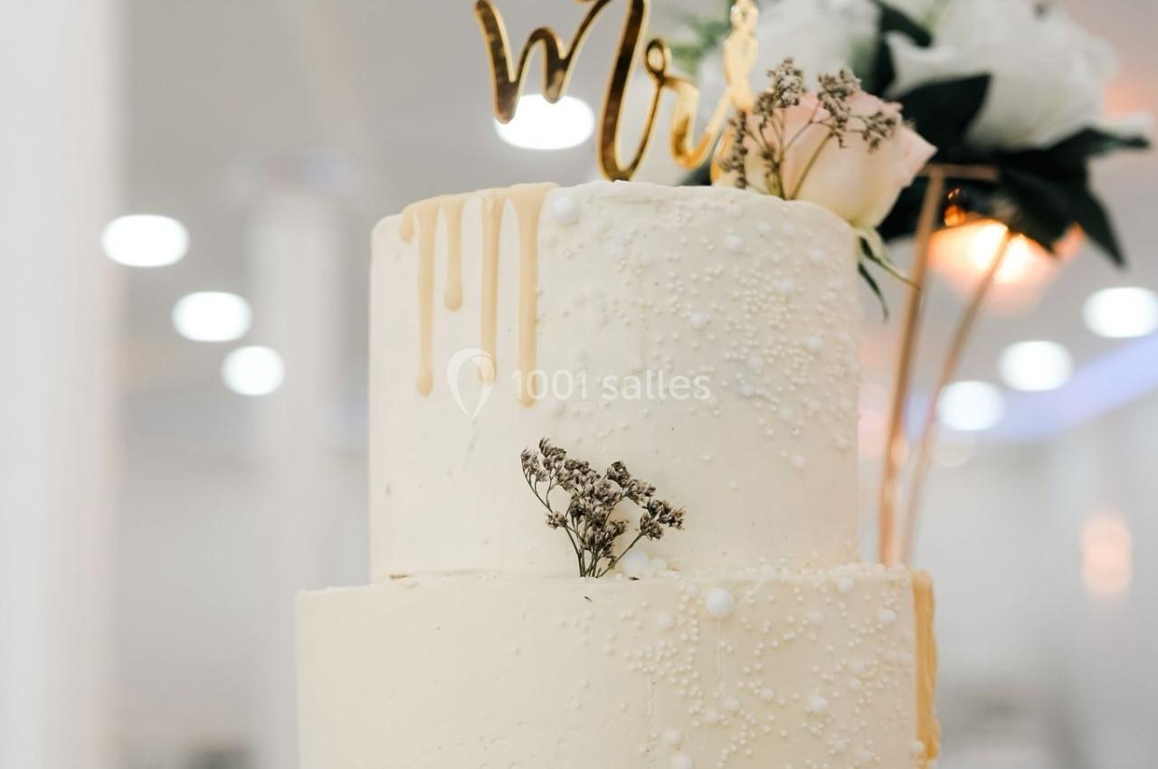 Gâteau de mariage à deux étages décoré de perles comestibles, fleurs et un topper ’Mr & Mrs’.