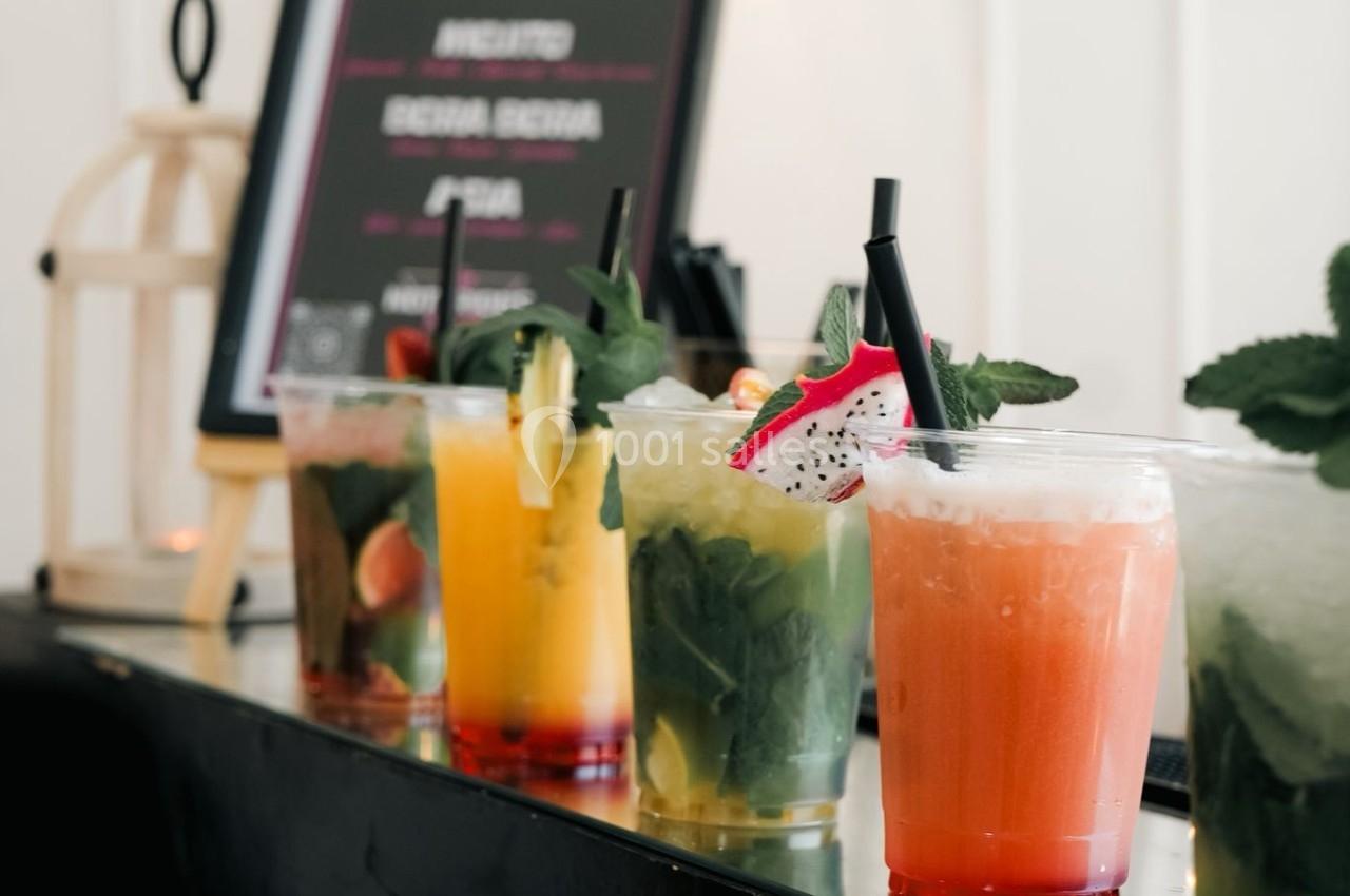Verres de cocktails variés avec garnitures colorées alignés sur un comptoir noir devant un panneau de menu.