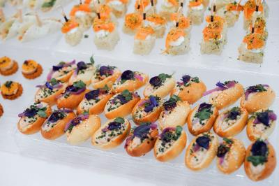 Salle de réception lumineuse avec tables rondes dressées, chaises blanches et buffets alignés sur le côté.