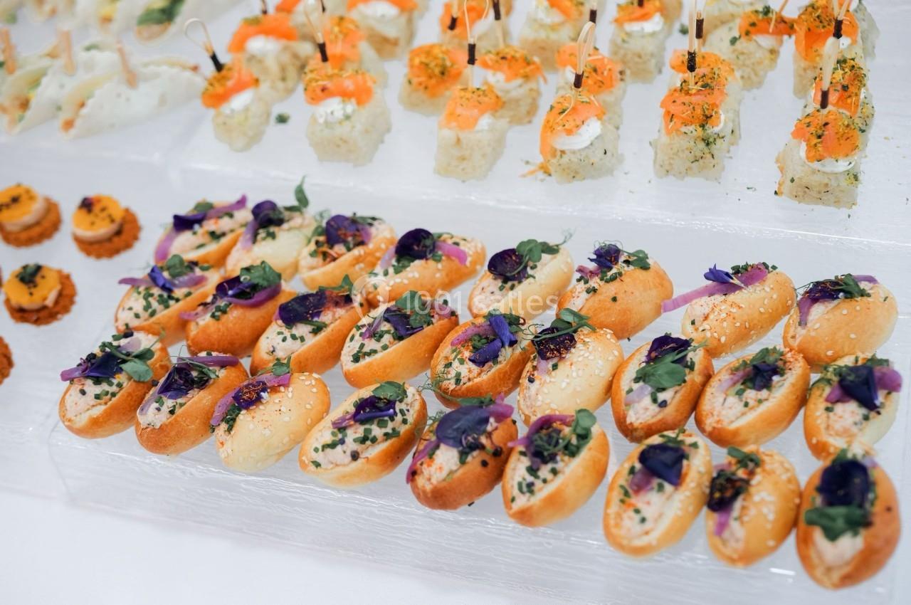Plateau de petits fours variés, incluant des bouchées garnies de fleurs comestibles et des sushis décorés.