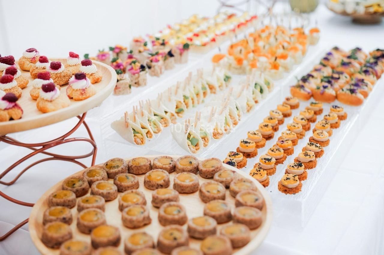Plateaux de bouchées apéritives variées disposées sur une table blanche, comprenant canapés, mini-sandwichs et amuse-bouches.