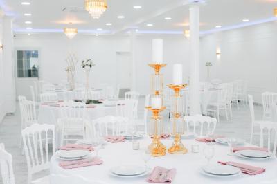 Salle de réception lumineuse avec tables rondes dressées, chaises blanches et buffets alignés sur le côté.