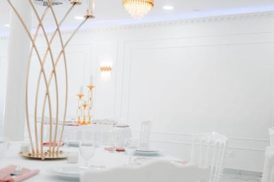 Salle de réception lumineuse avec tables rondes dressées, chaises blanches et buffets alignés sur le côté.