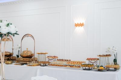 Salle de réception lumineuse avec tables rondes dressées, chaises blanches et buffets alignés sur le côté.