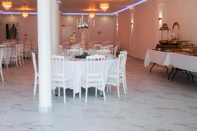 Salle de réception lumineuse avec tables rondes dressées, chaises blanches et buffets alignés sur le côté.