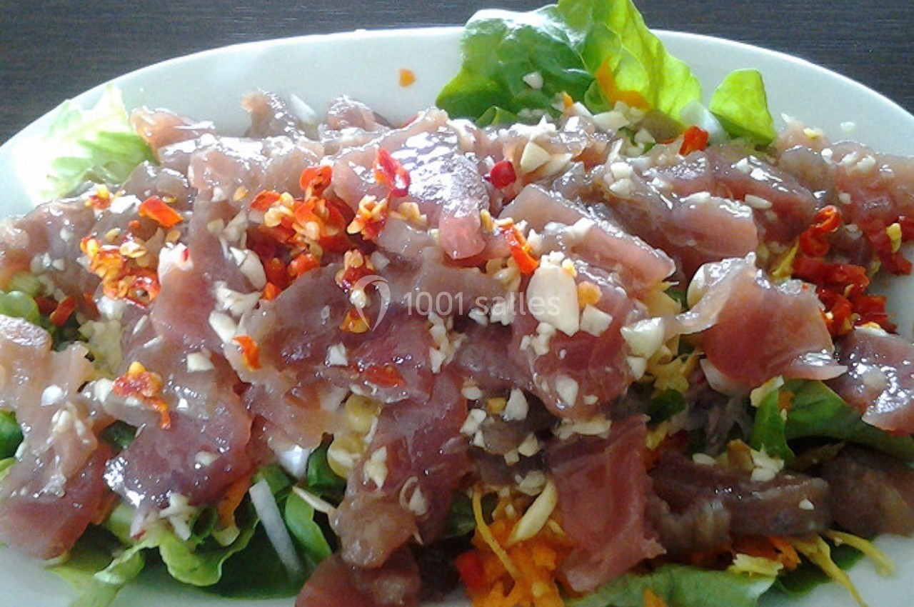 Assiette de salade garnie de morceaux de poisson cru, piments rouges hachés et ail, servie sur des feuilles de laitue.