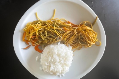 Assiette contenant des nouilles sautées aux légumes et une portion de riz blanc, posée sur une table noire.