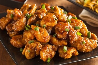 Morceaux de poulet frit nappés de sauce brillante, garnis de ciboulette, servis sur une assiette noire.