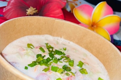 Bol en carton rempli d'une préparation crémeuse garnie de ciboulette, avec des fleurs tropicales en arrière-plan.