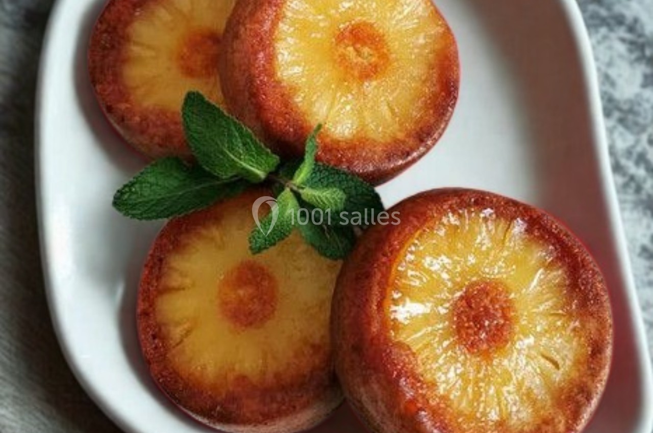 Tranches d'ananas caramélisées disposées sur un plat blanc, décorées de feuilles de menthe fraîche.