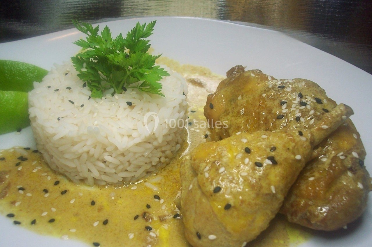 Plat de poulet au curry avec sauce, riz blanc décoré de persil et graines de sésame, accompagné de quartiers de citron vert.