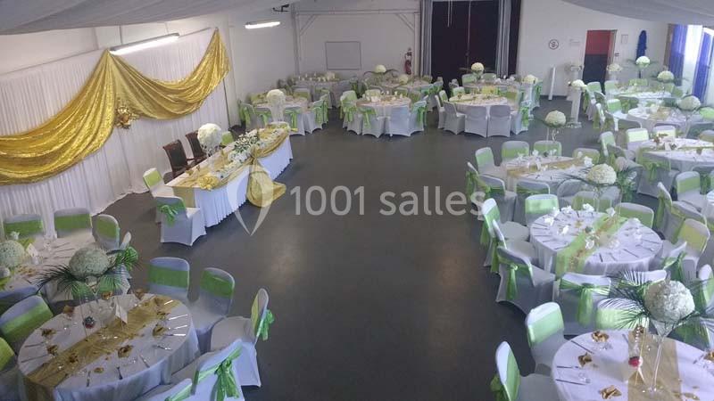Salle de réception décorée avec des nappes blanches, des rubans verts et dorés, et des centres de table fleuris.