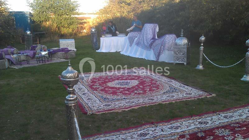 Espace extérieur décoré de tapis, lanternes et coussins, avec une table dressée en arrière-plan.