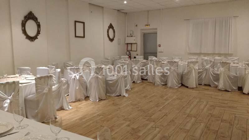 Salle de réception avec des chaises blanches décorées de nœuds, disposées autour de tables sur un sol en parquet clair.