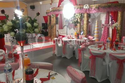 Espace extérieur décoré de tapis, lanternes et coussins, avec une table dressée en arrière-plan.