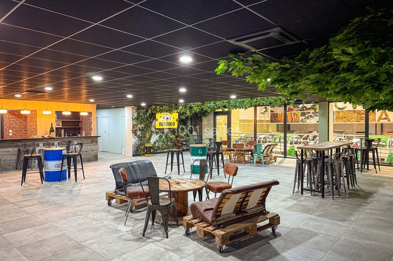 Espace intérieur aménagé avec des tables hautes, des fauteuils en palettes et une décoration végétale.