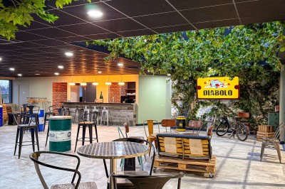 Salle intérieure avec tables hautes, tabourets noirs et plafond décoré de feuillage, donnant sur une vitrine lumineuse.