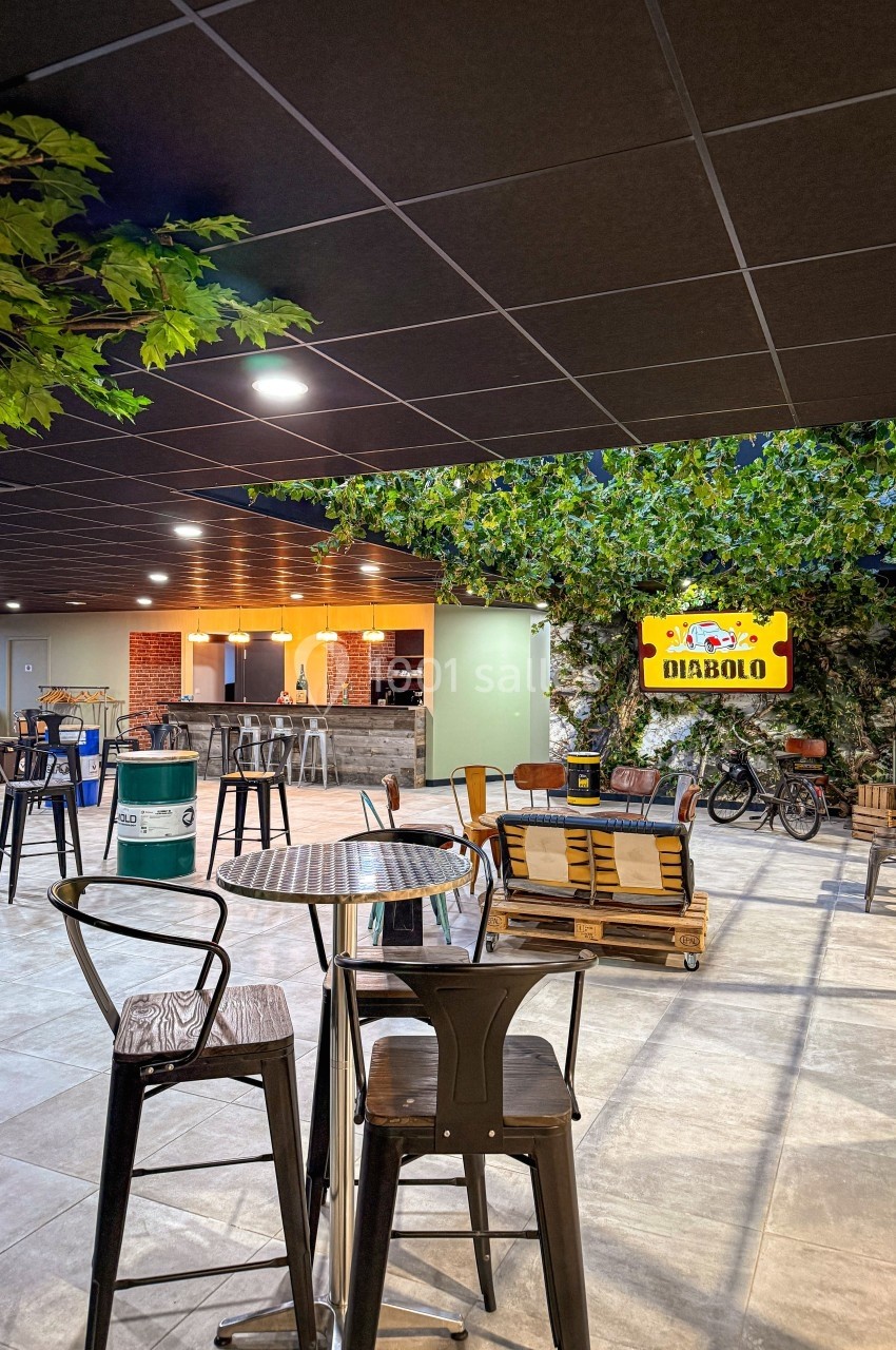 Espace intérieur avec tables, chaises, bar éclairé et décoration végétale, ambiance conviviale et moderne.