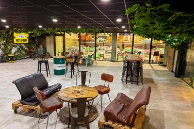 Salle intérieure avec tables hautes, tabourets noirs et plafond décoré de feuillage, donnant sur une vitrine lumineuse.