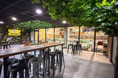 Salle intérieure avec tables hautes, tabourets noirs et plafond décoré de feuillage, donnant sur une vitrine lumineuse.