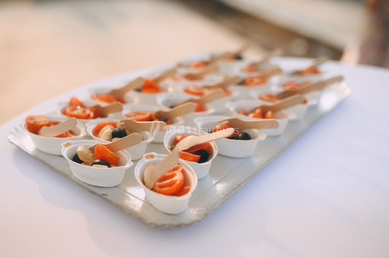 Petites verrines contenant des tranches de saumon, olives noires et cuillères en bois, disposées sur un plateau.