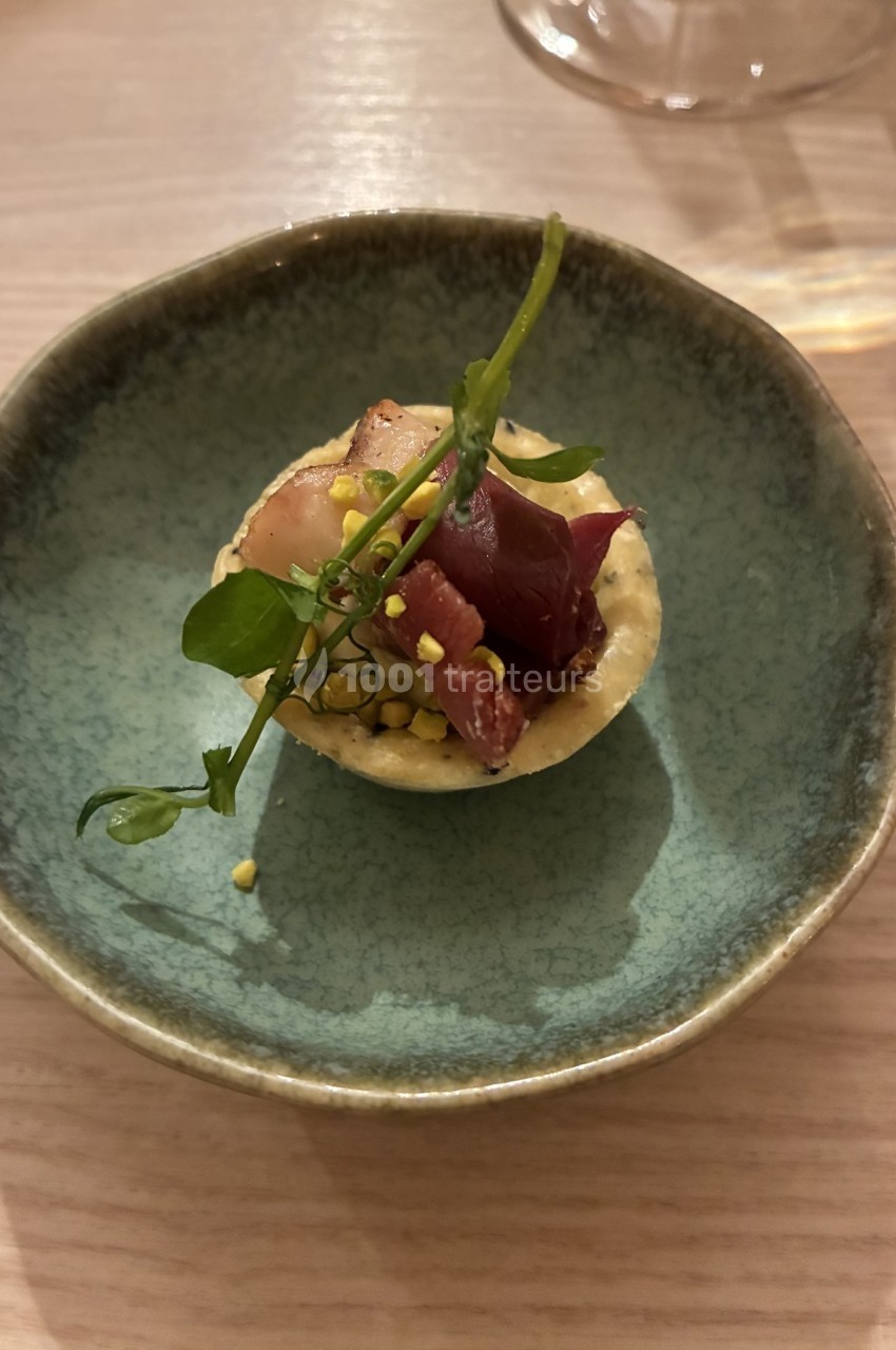 Tartelette garnie de morceaux de viande, herbes fraîches et éclats croquants, présentée dans une assiette en céramique.