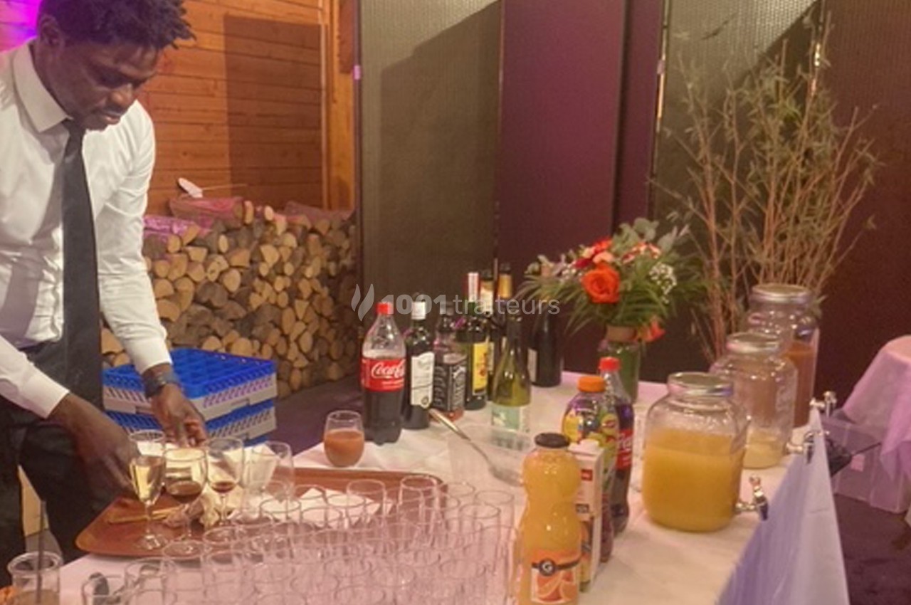 Un serveur prépare des verres de champagne sur un plateau, devant une table garnie de boissons et de décorations.