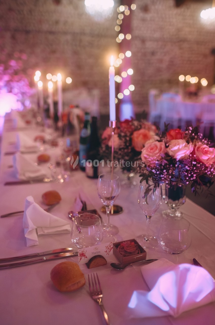Table de réception élégamment dressée avec bougies, fleurs roses, verres et couverts dans une ambiance tamisée.