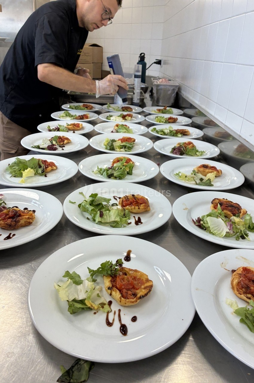 Un chef prépare des assiettes contenant des tartelettes aux légumes et de la salade verte dans une cuisine professionnelle.