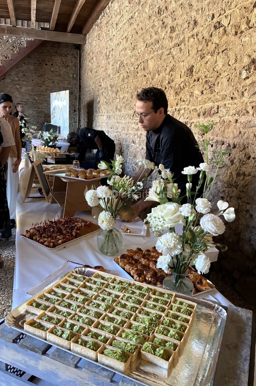 Un traiteur prépare un buffet avec des fleurs blanches en décoration dans une salle aux murs en pierre.