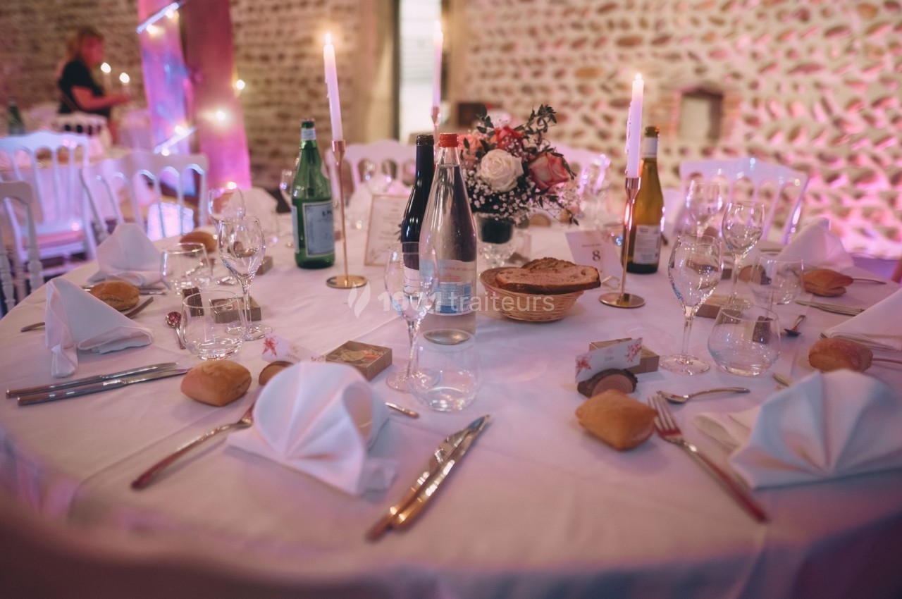 Table dressée pour un repas festif avec nappes blanches, couverts, verres, bougies et décoration florale.