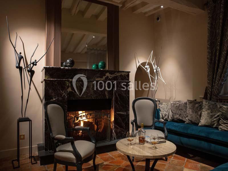 Cheminée en marbre allumée dans un salon élégant avec fauteuils, table basse et sculptures modernes.