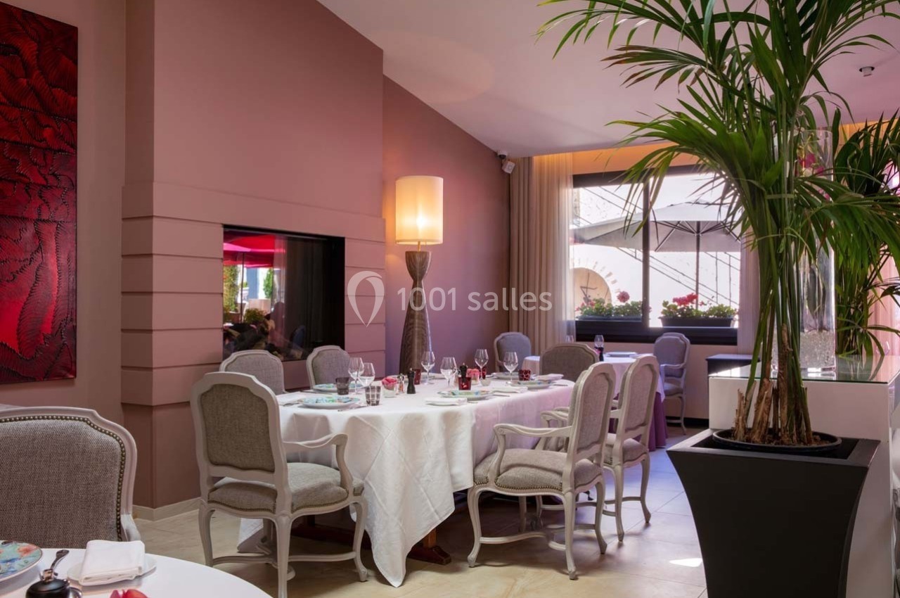 Salle de restaurant élégante avec tables dressées, chaises rembourrées, grande plante et lumière naturelle.