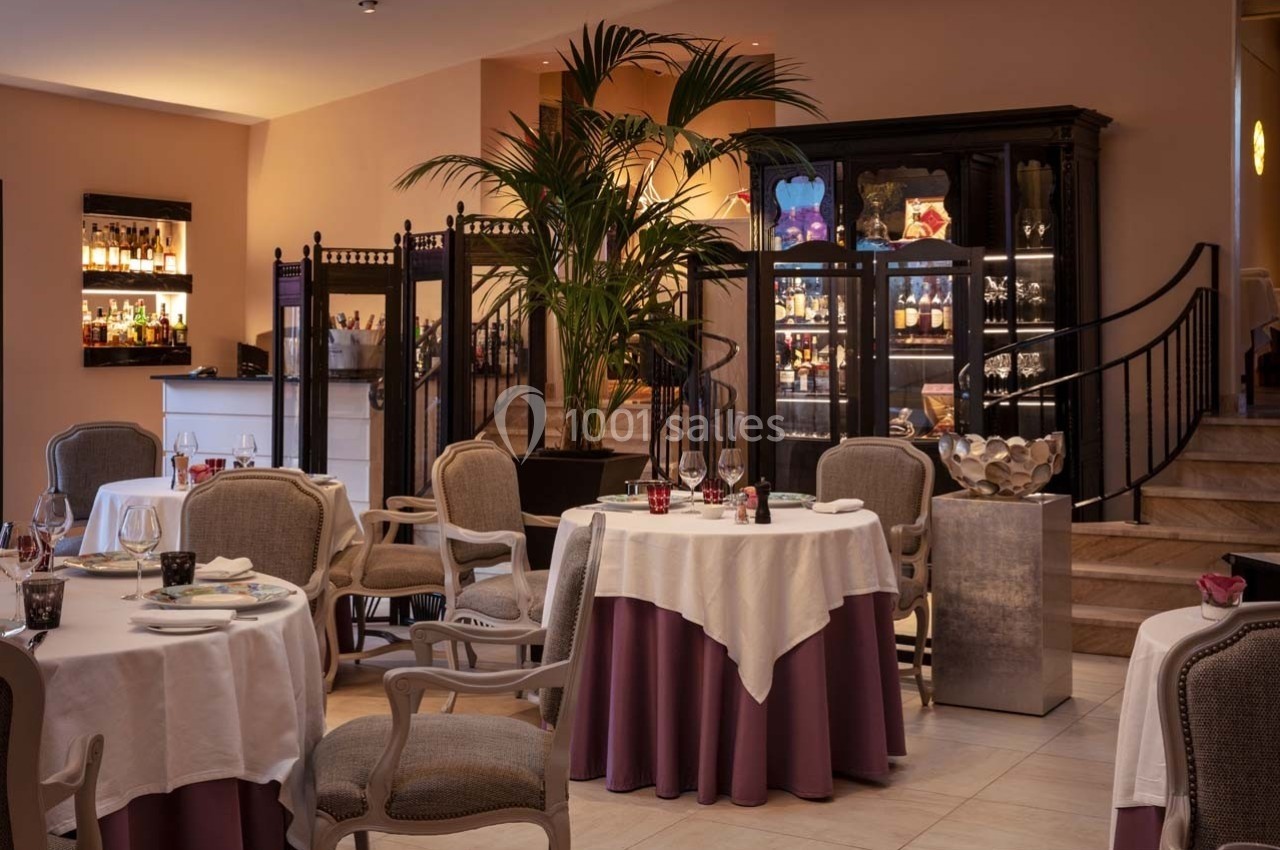 Salle de restaurant élégante avec tables dressées, chaises classiques, éclairage tamisé et vitrines en arrière-plan.