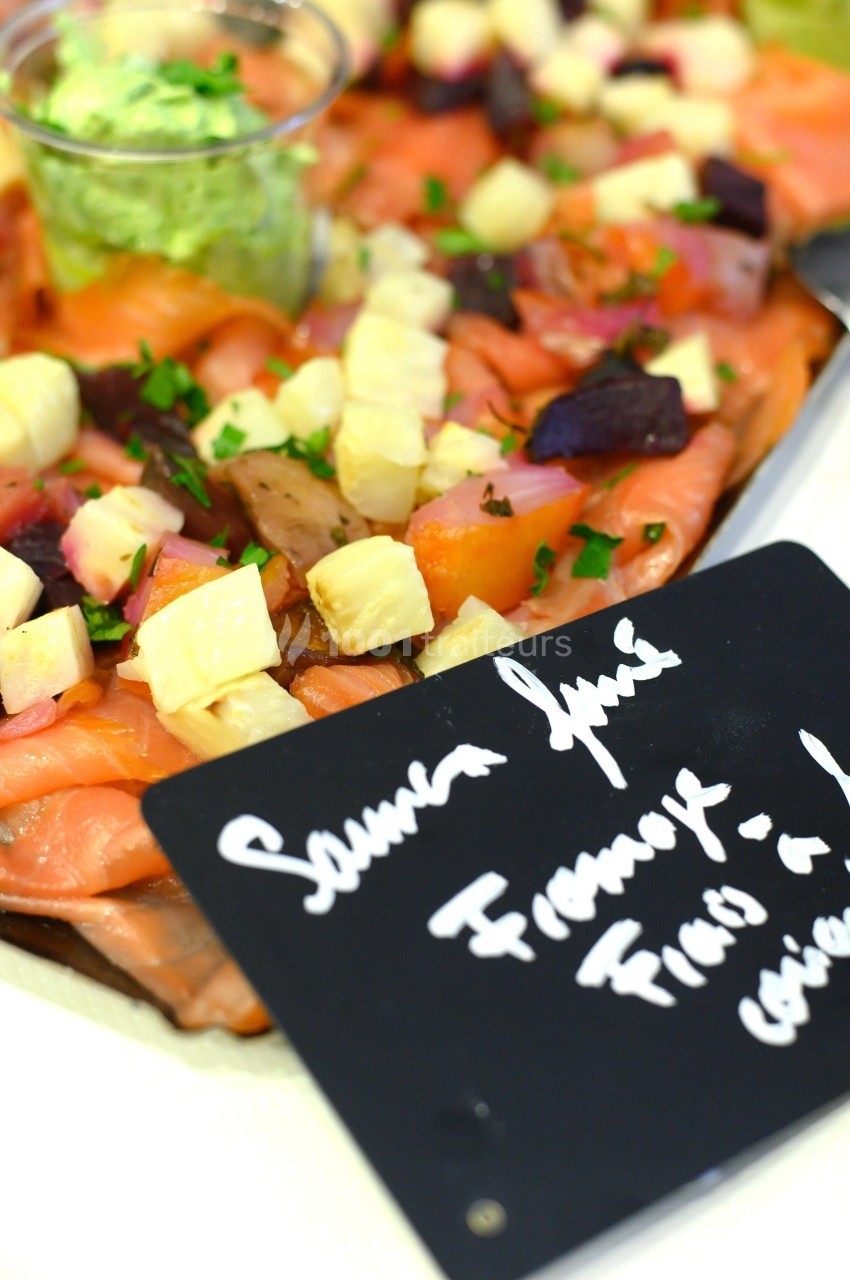 Assiette de saumon fumé garnie de dés de fromage, betteraves et persil, avec une sauce verte en accompagnement.