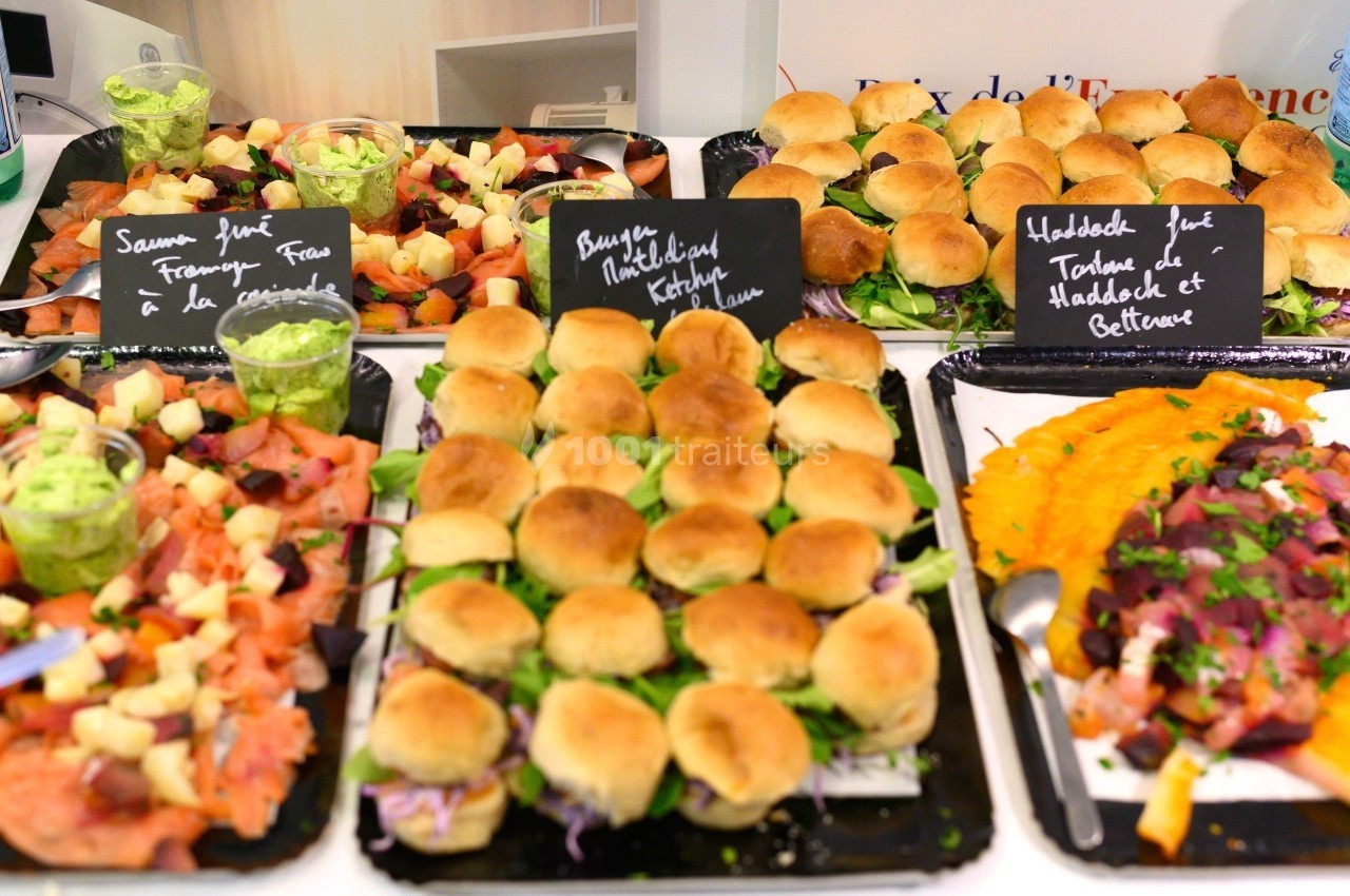 Plateaux de mini-burgers, toasts garnis et salades colorées présentés sur un buffet.