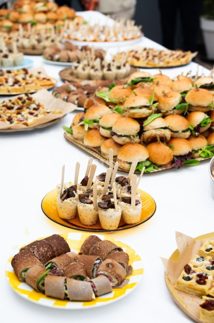 Buffet avec mini-sandwichs, roulés, verrines et autres amuse-bouches disposés sur une table blanche.
