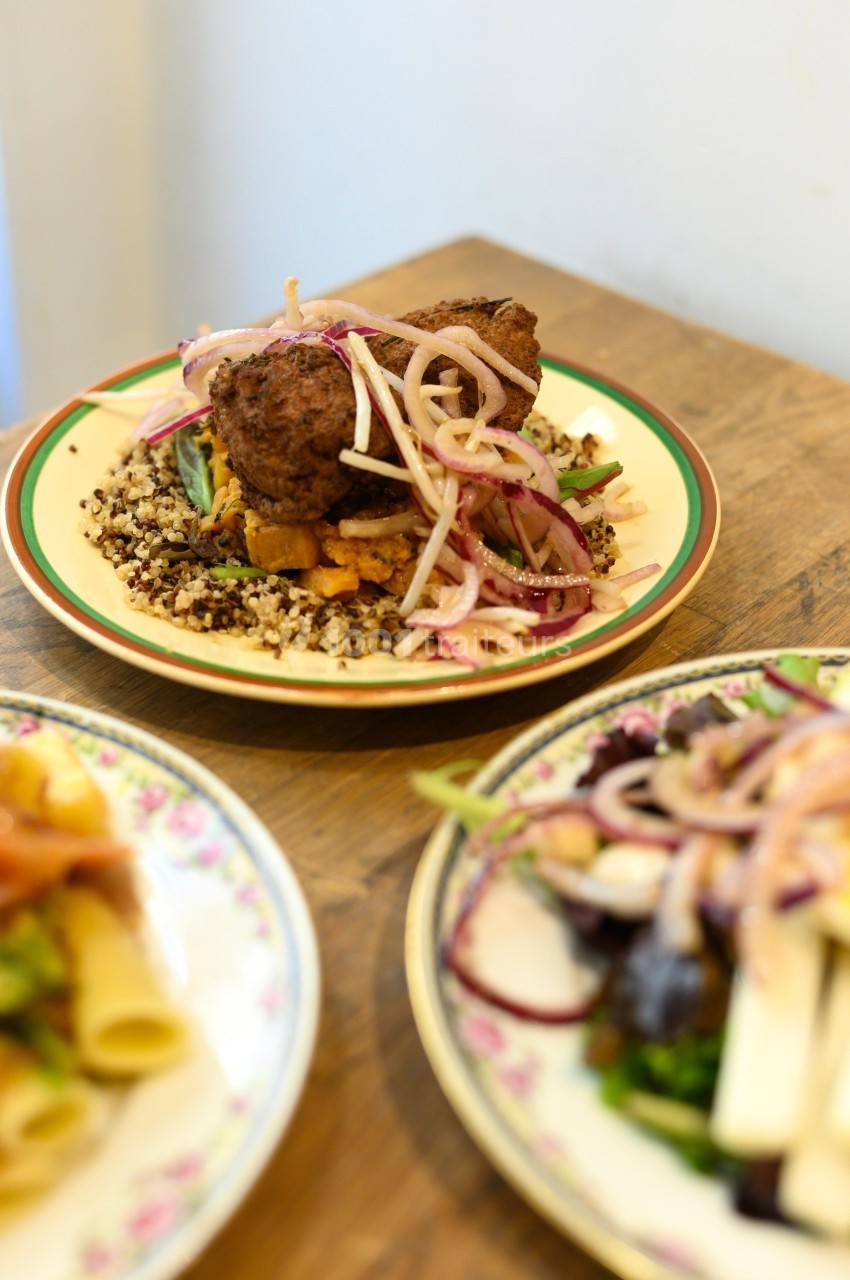 Assiette de boulettes de viande servies sur un lit de quinoa avec des légumes et des oignons rouges marinés.