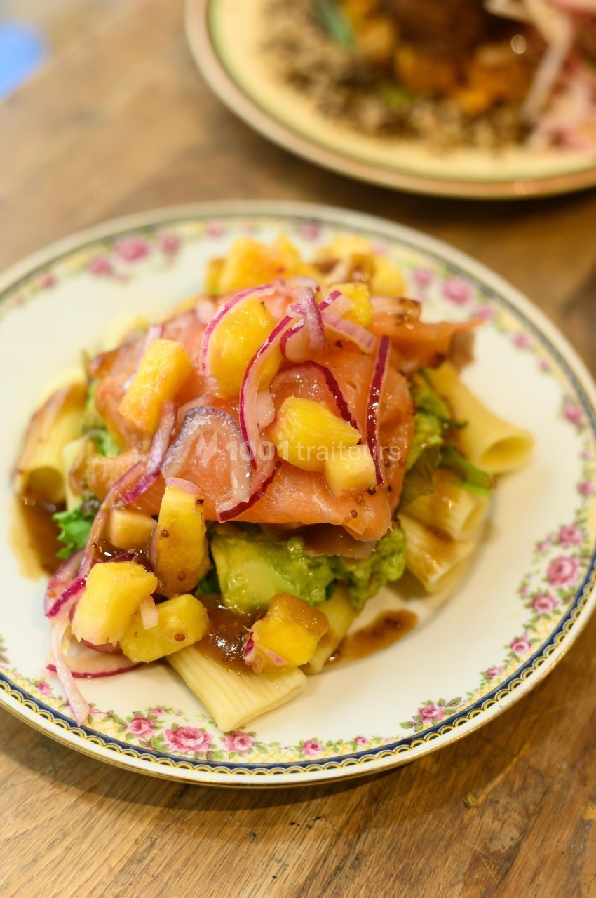 Assiette de pâtes garnie de saumon fumé, morceaux d'ananas, oignons rouges et sauce, servie sur une table en bois.