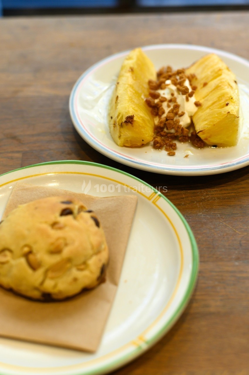 Assiette avec ananas frais, yaourt et granola, à côté d'un cookie aux pépites de chocolat sur une serviette.
