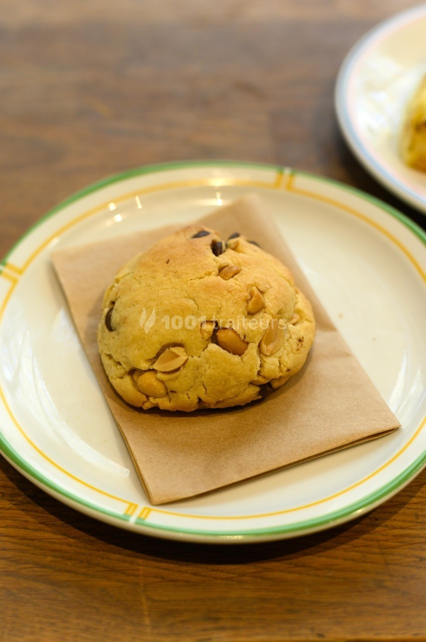 Cookie aux pépites de chocolat et noix de macadamia posé sur une serviette dans une assiette blanche.