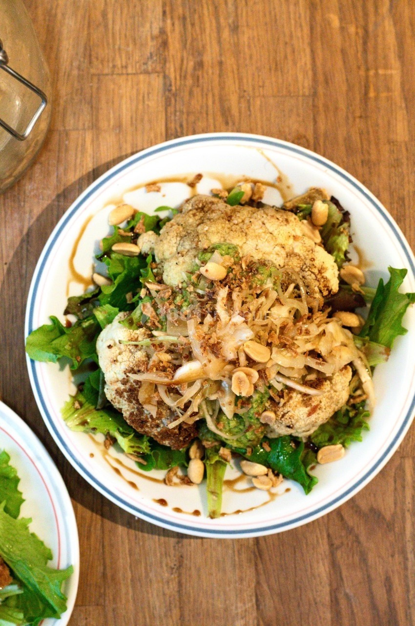 Assiette de chou-fleur rôti sur un lit de salade verte, garnie de cacahuètes, oignons frits et sauce.
