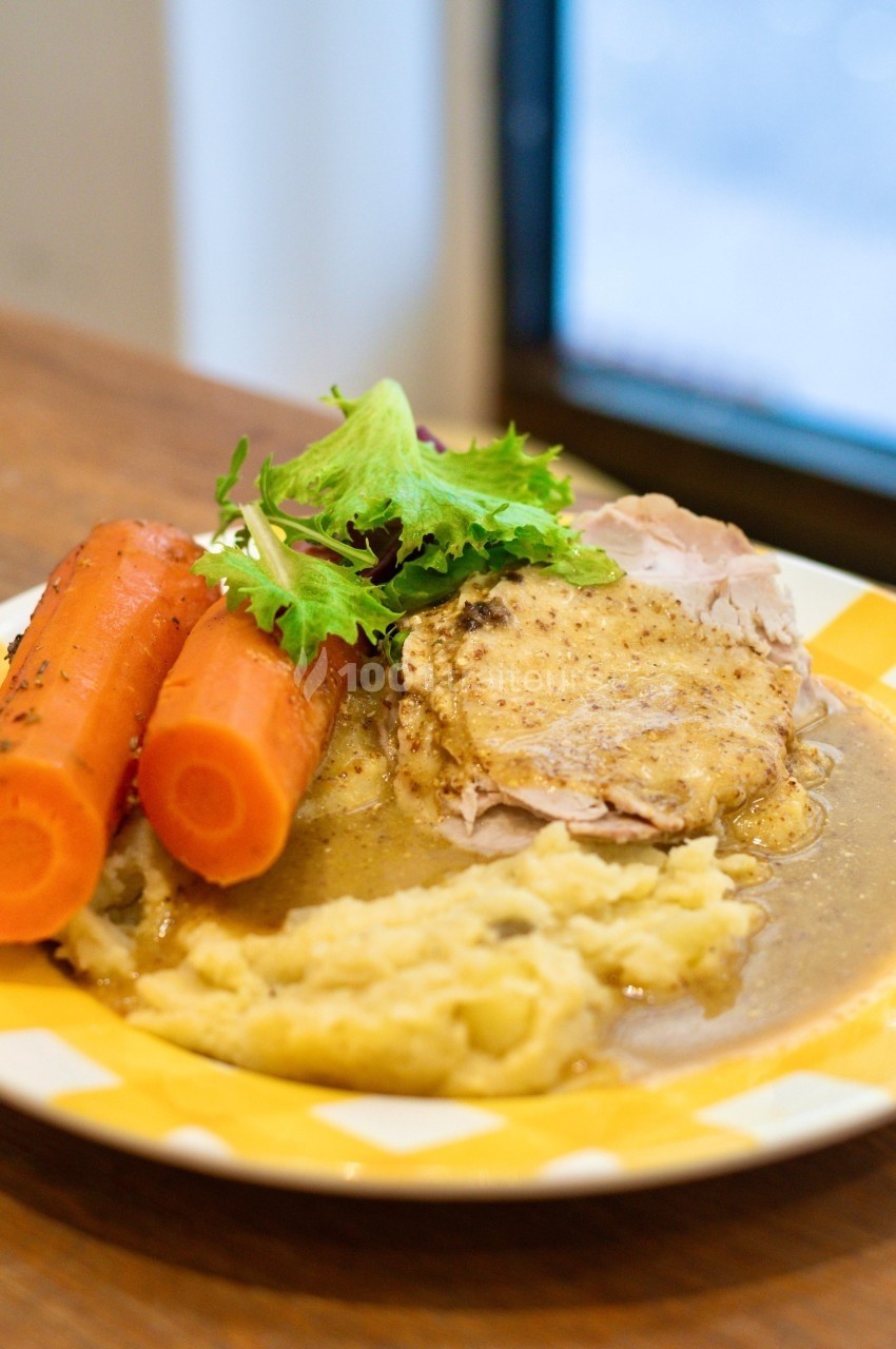 Assiette contenant de la purée, des carottes cuites, des tranches de viande en sauce et une garniture de salade verte.